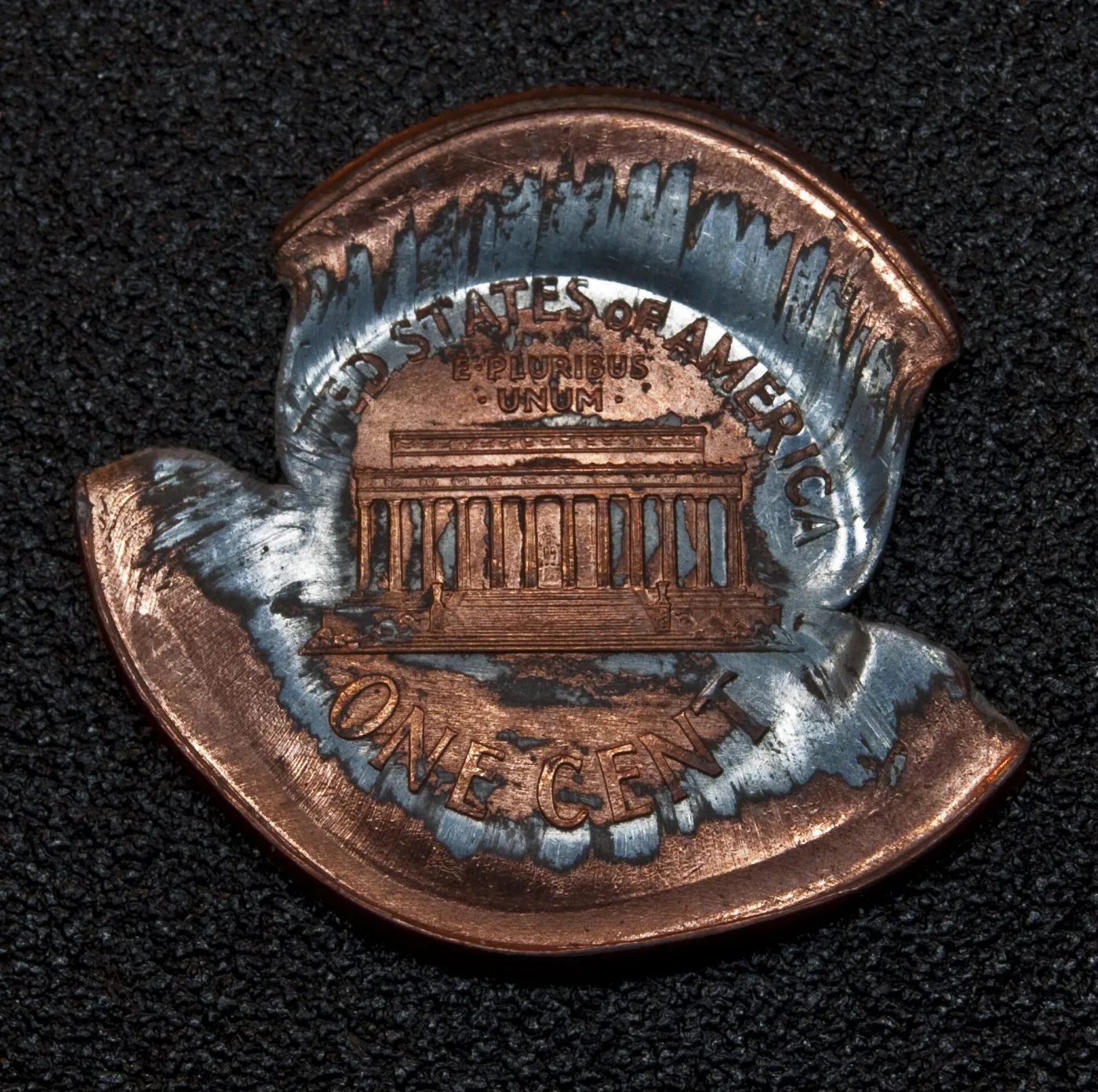 Badly misshapen Lincoln Memorial cent with the copper plating stretched away to show the grey zinc core around the lettering