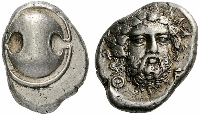 Obverse and reverse of a silver stater of Thebes, an oval shield with scooped sides, and a bearded head of Dionysos facing the viewer