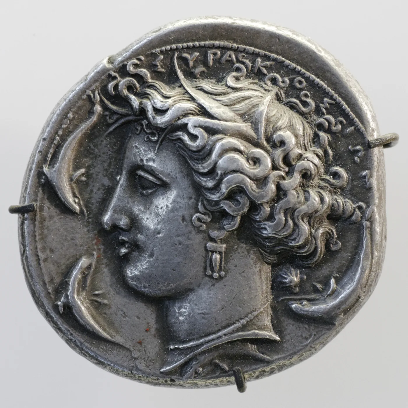 Silver decadrachm of Syracuse, the head of the nymph Arethusa facing left with flowing hair, dolphins swimming around her and Greek lettering above