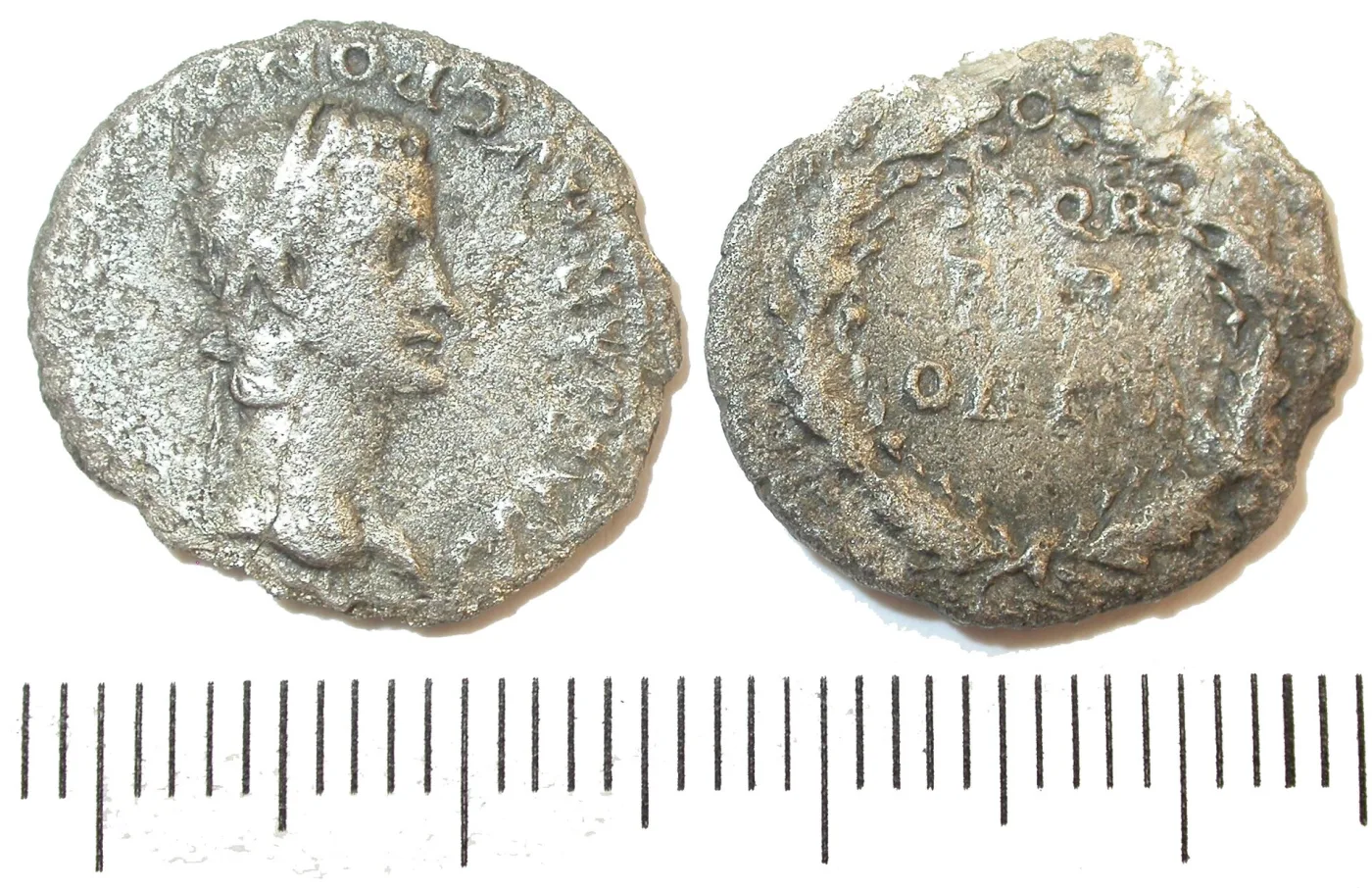 Obverse and reverse of a worn silver denarius of Caligula photographed side by side above a millimetre scale, the reverse showing an inscription inside a wreath