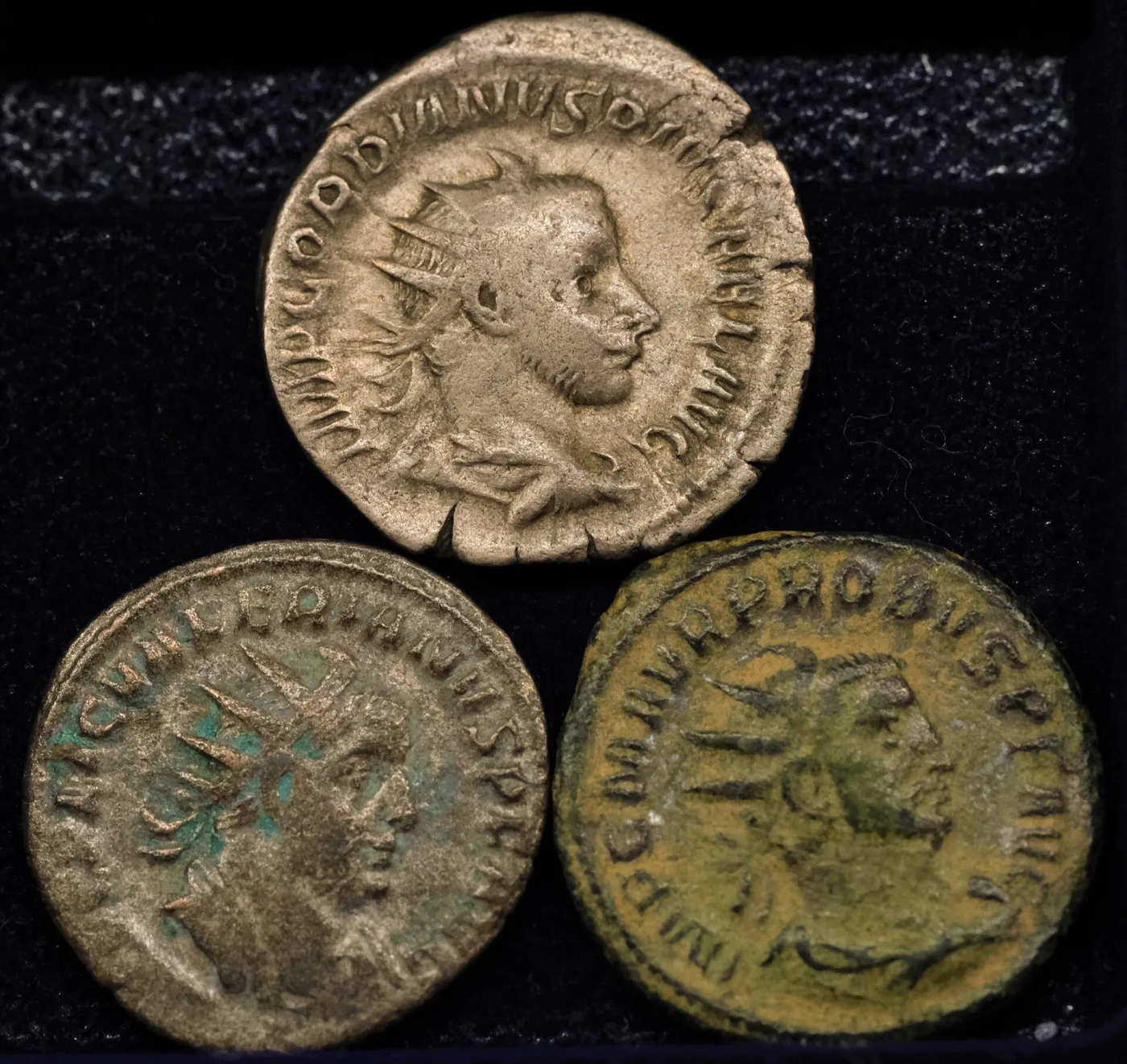 Three Roman antoniniani side by side, the largest bright silver, the second smaller and grey, the third small and green bronze