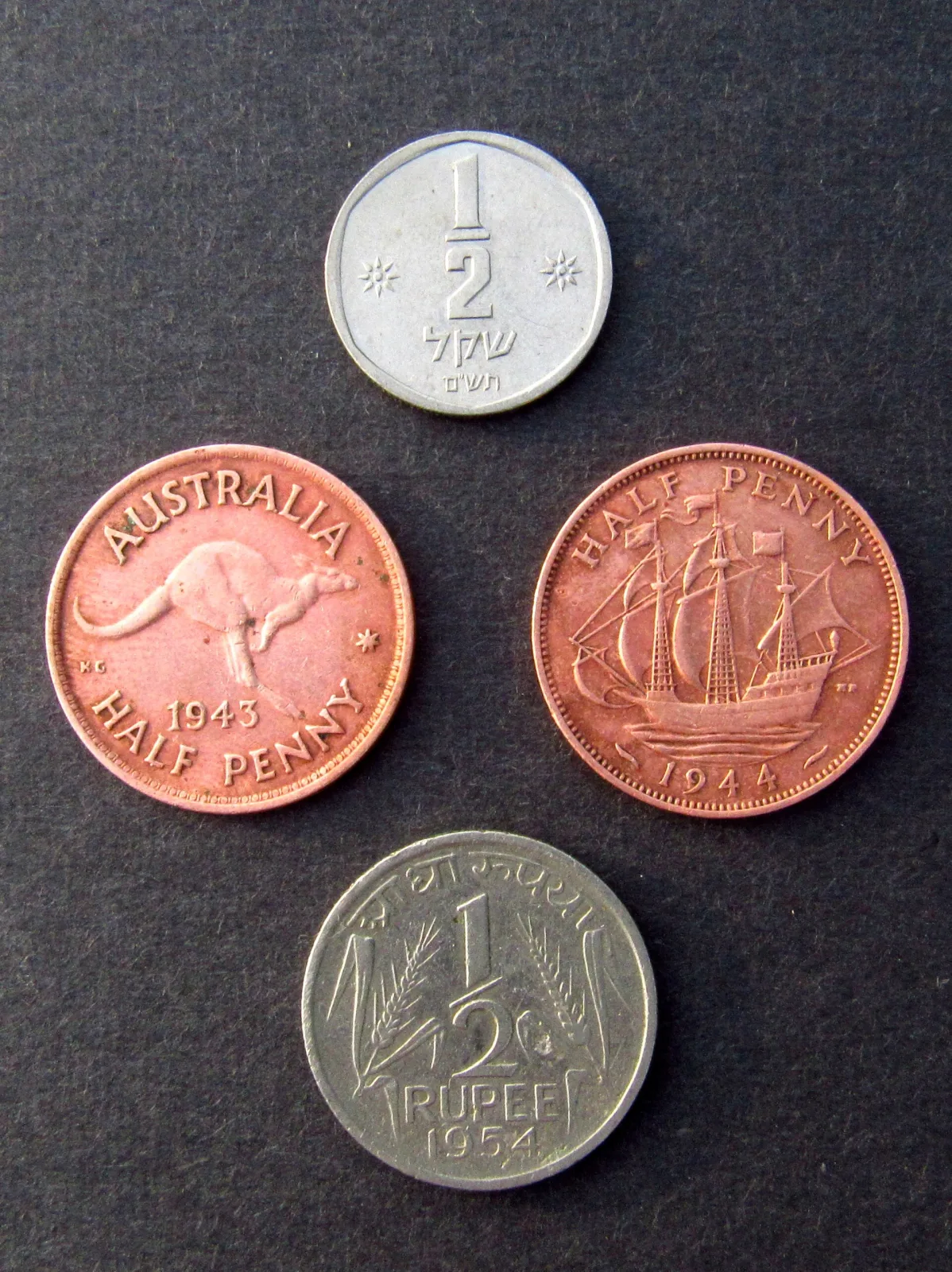 Four small coins arranged on a dark surface, including a bronze Australian halfpenny with a kangaroo and a bronze British halfpenny with a sailing ship
