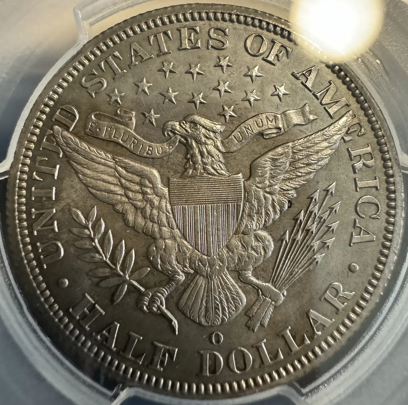 Close-up reverse of an 1894-O Barber half dollar with a small oval O mint mark below the eagle's tail feathers and above the HALF DOLLAR legend