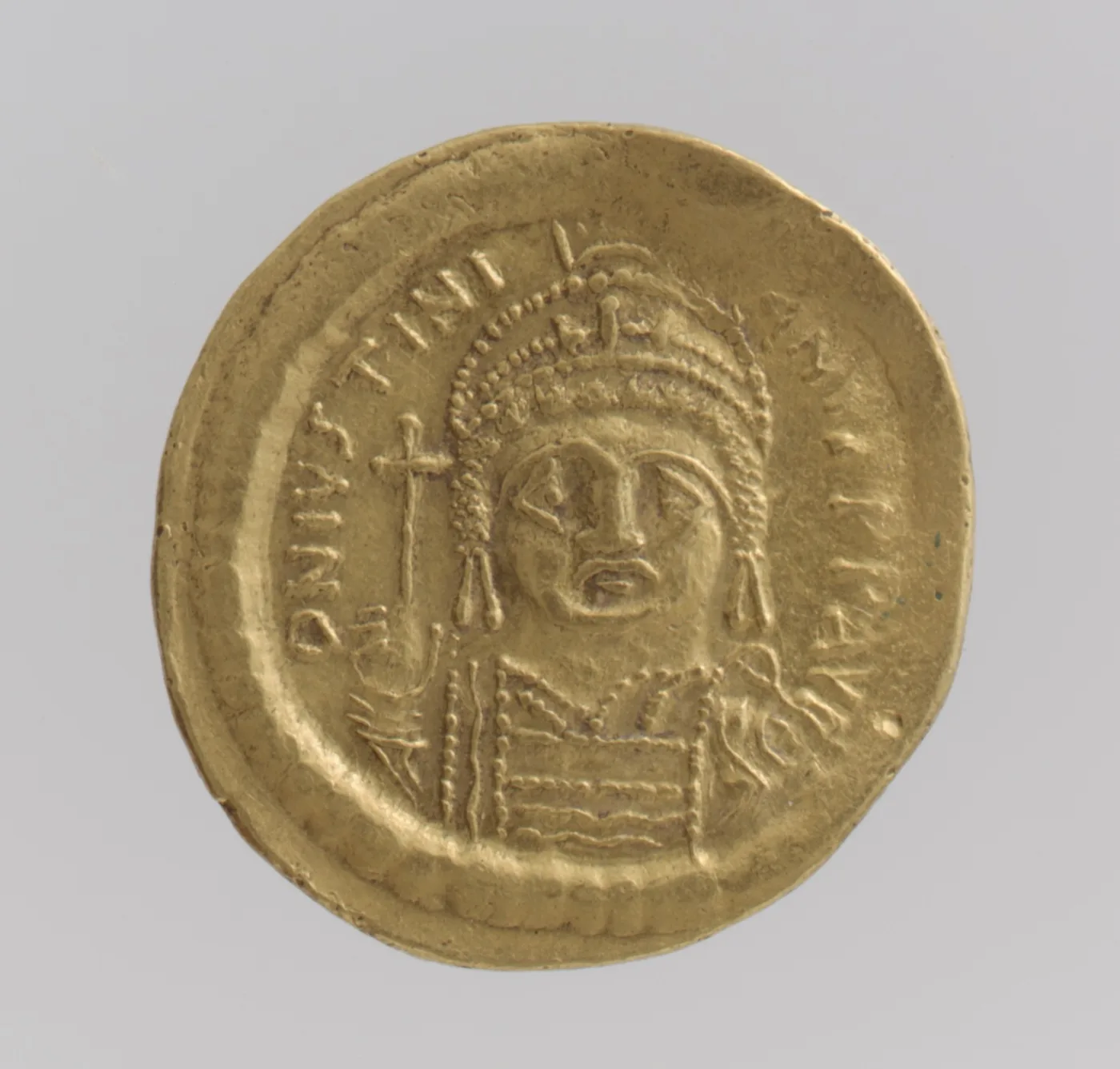 Obverse of a Byzantine gold solidus of Justinian I, a helmeted bust facing the viewer holding a globe surmounted by a cross