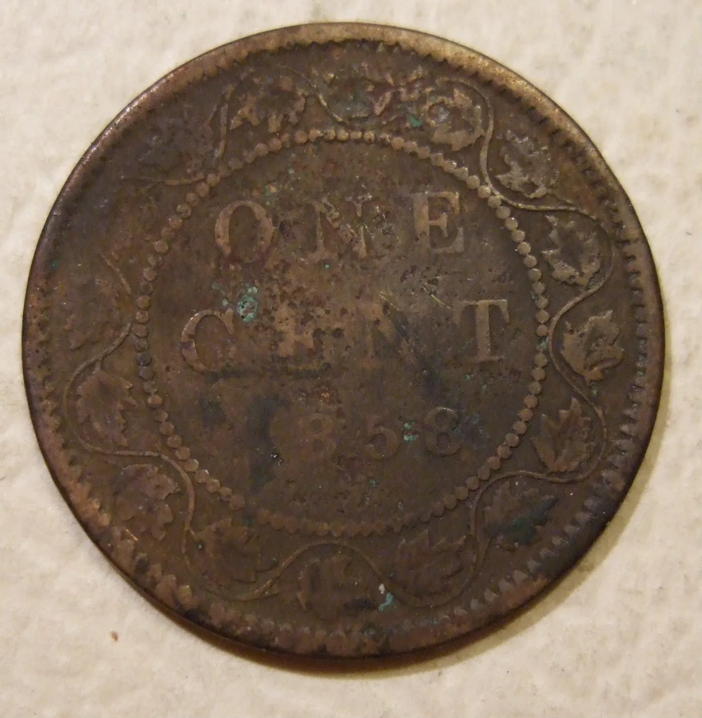 A worn brown Canadian one cent coin with the words ONE CENT in a beaded circle and the date 1858 below