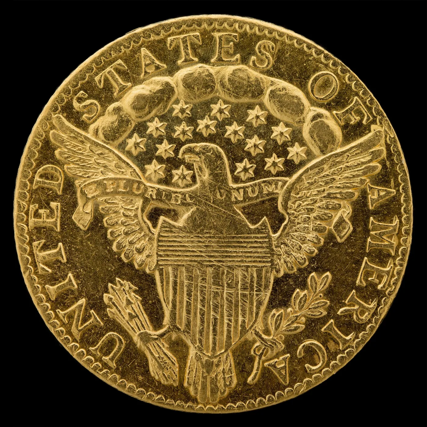 Reverse of an 1796 quarter eagle showing a heraldic eagle with a striped federal shield on its breast, E PLURIBUS UNUM on a scroll, clouds and stars above the eagle, and no statement of value