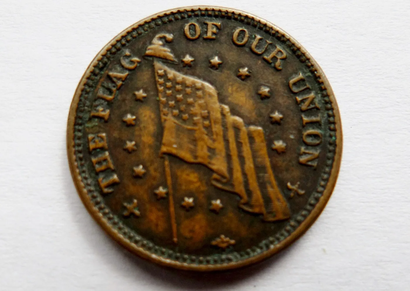 Close view of the flag side of a Dix Civil War token, showing the waving national flag ringed by stars and the legend THE FLAG OF OUR UNION