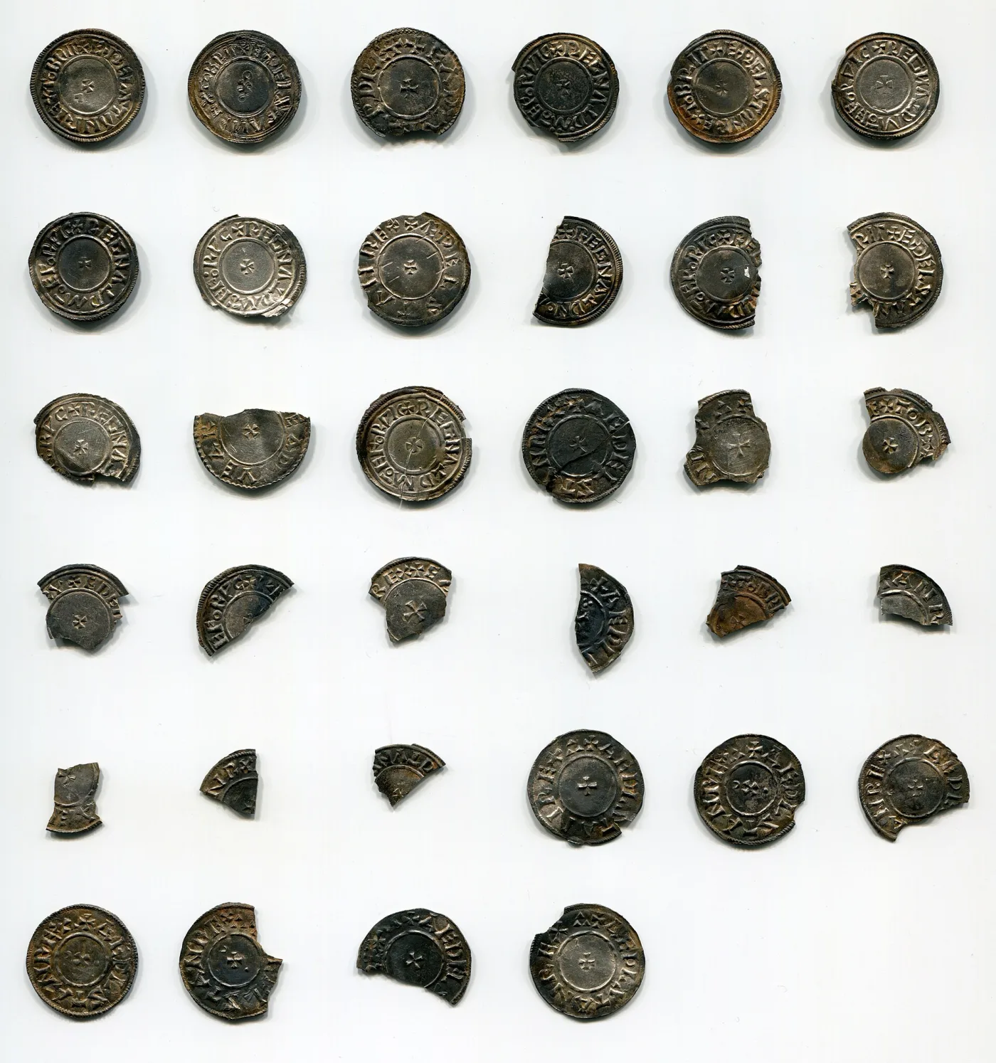 A group of about thirty small medieval silver coins and fragments laid out on a white background, many broken or clipped