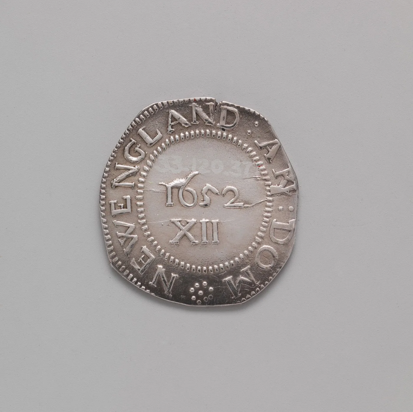 Reverse of a 1652 Massachusetts Pine Tree shilling showing NEW ENGLAND AN DOM around the rim and the date 1652 above the Roman numeral XII