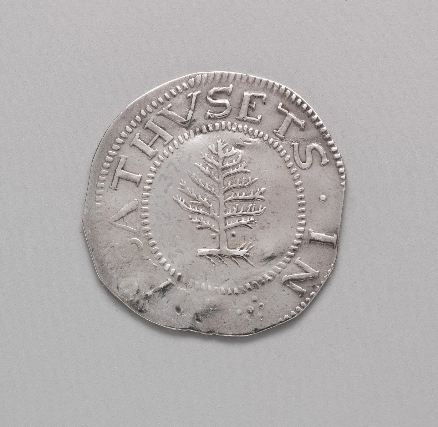 Obverse of a 1652 Massachusetts Pine Tree shilling showing the tree inside a beaded circle with the legend MASATHVSETS IN around the rim