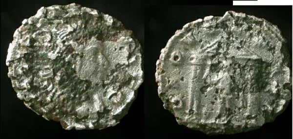 Two faces of a small Roman coin whose surface has broken away in places to reveal a darker core beneath a thin lighter skin