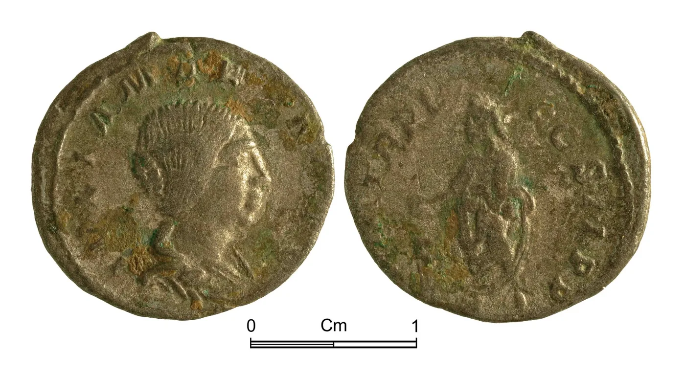 Two faces of a Roman denarius with soft, slightly blurred detail and a rough granular surface, photographed beside a scale