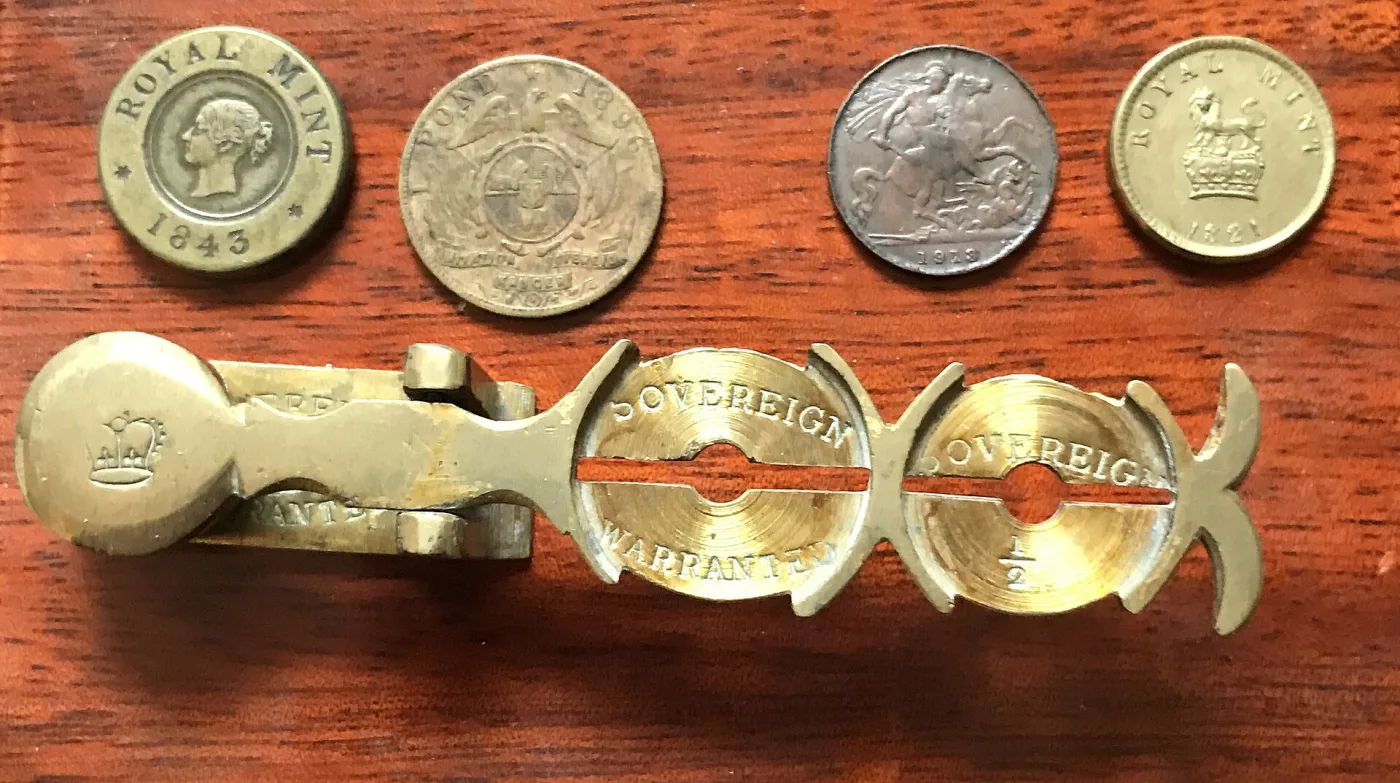 A nineteenth-century folding sovereign balance for detecting false gold coins, shown with two coin weights
