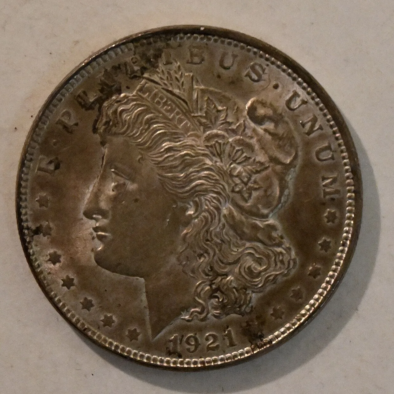 Obverse of a toned 1921 Morgan silver dollar, Liberty facing left in a cap with wheat and cotton, LIBERTY on the headband and E PLURIBUS UNUM above