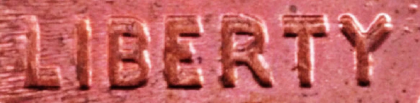 Extreme close-up of the word LIBERTY on a Lincoln cent, each letter showing a distinct doubled edge