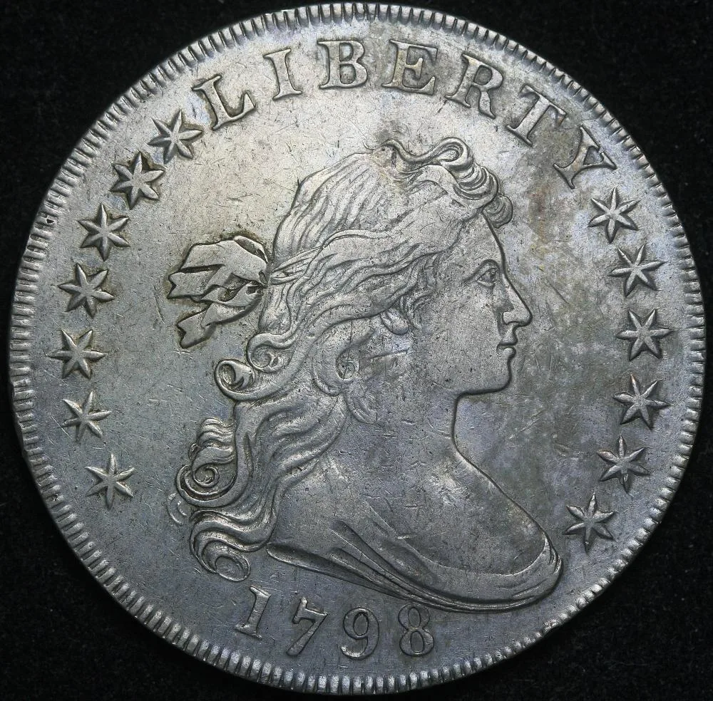 Obverse of a 1798 Draped Bust dollar on a black background showing thirteen stars, seven to the left of Liberty and six to the right, above a bold 1798 date
