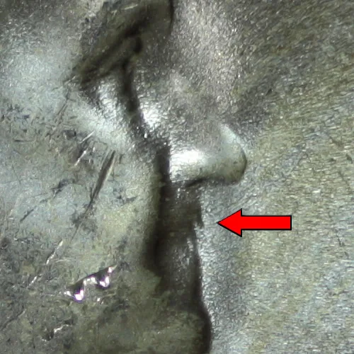Macro view of the mouth of a 1955 Bugs Bunny Franklin half dollar, a red arrow pointing at two raised marks projecting downward from the upper lip