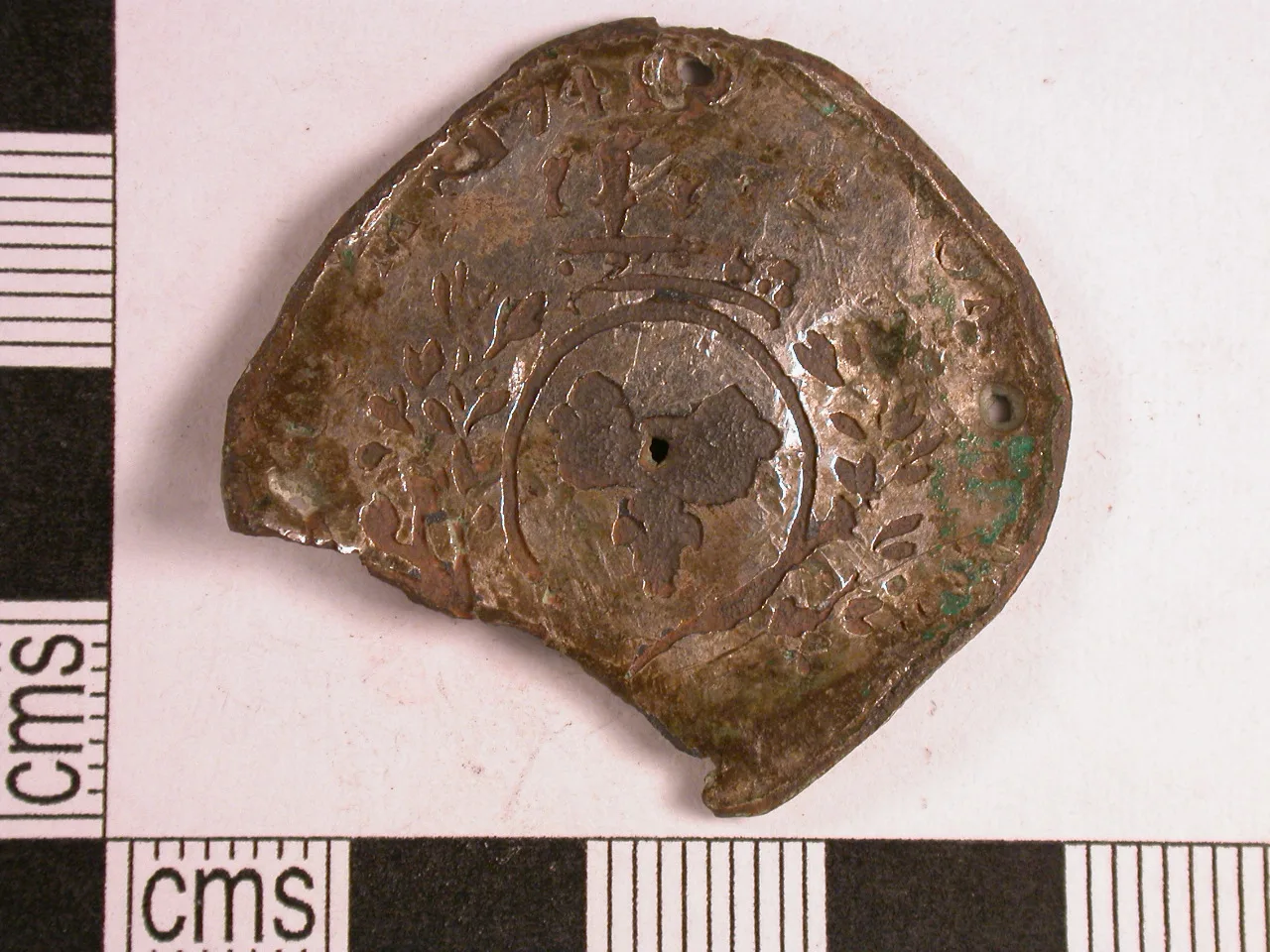 Corroded base-metal copy of a half ecu of Louis XV, photographed against a centimetre scale, with the crowned arms still legible under green corrosion
