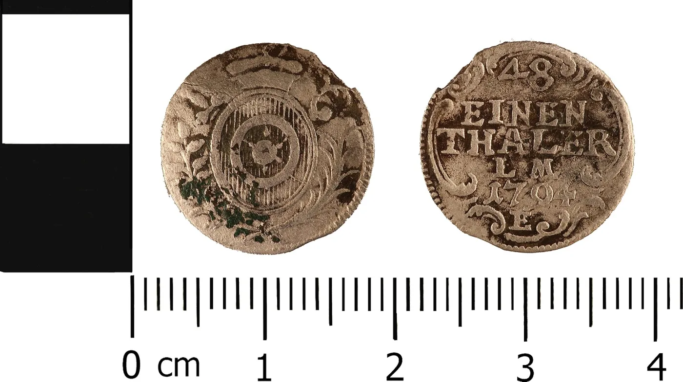 Both sides of a small worn silver coin of 1704 photographed against a centimetre scale, the right side reading 48 EINEN THALER above the date