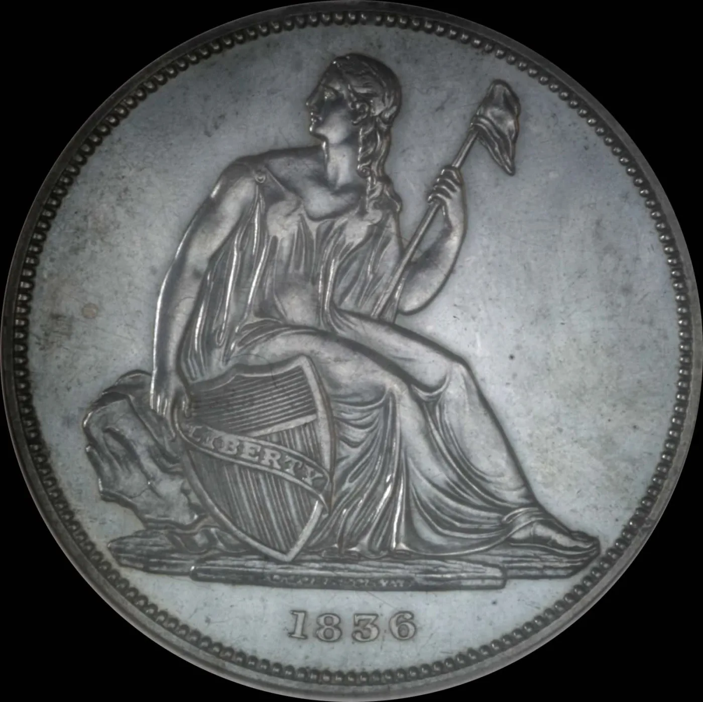 Obverse of an 1836 Gobrecht dollar showing Liberty seated on a rock with a shield lettered LIBERTY and a capped pole, in an empty field with no stars