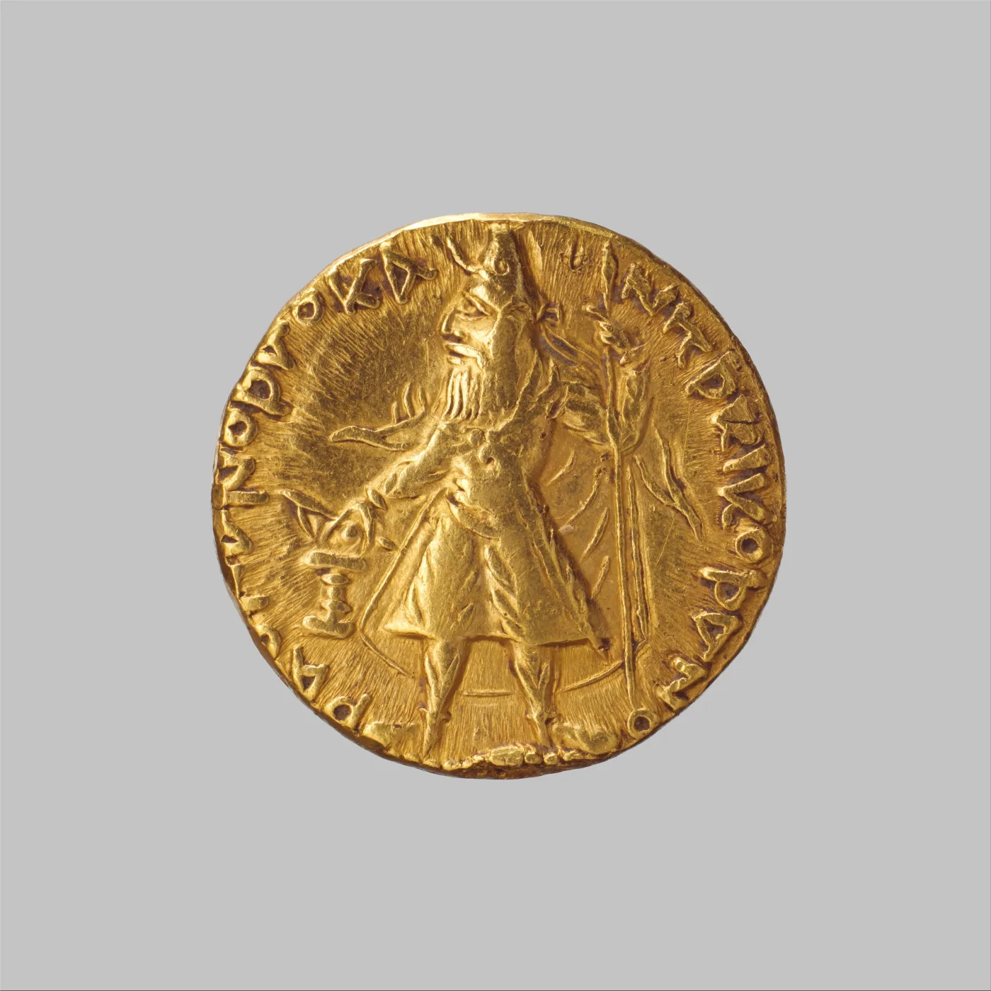 Kushan gold dinara of Kanishka I showing the bearded king standing at a fire altar wearing a heavy coat and trousers, with a Greek-letter legend around the edge