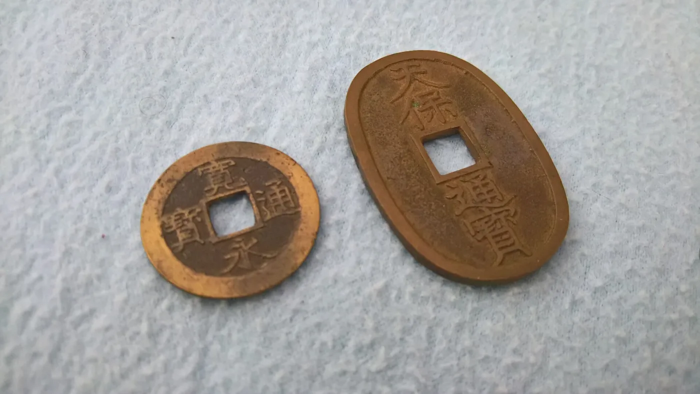 A round brass four-mon Kan'ei Tsuho with a square central hole beside the much larger oval Tenpo Tsuho hundred-mon coin