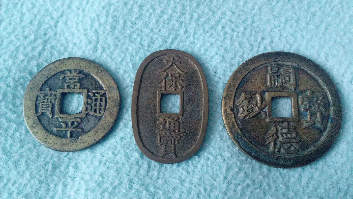 A round Korean Sangpyeong Tongbo, an oval Japanese Tenpo Tsuho and a large round Vietnamese cash coin photographed side by side