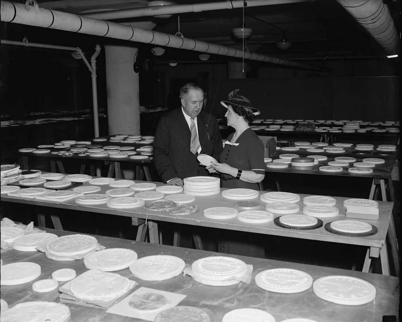 Two officials in 1938 examining large circular plaster relief models laid out across trestle tables during the judging of the new nickel design