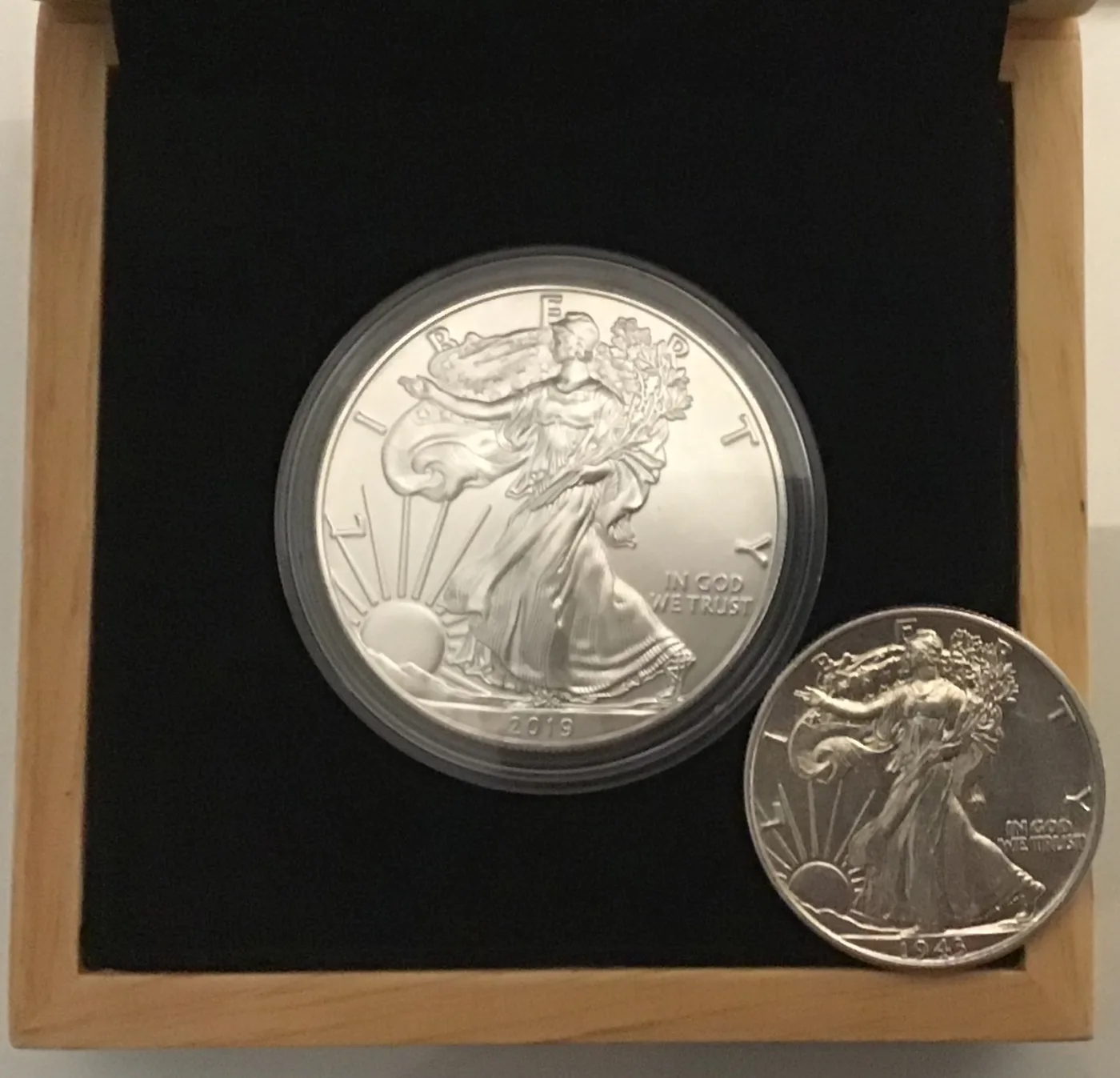 A 2019 American Silver Eagle in a capsule beside a 1943 Walking Liberty half dollar, both carrying Weinman's striding Liberty design at very different sizes