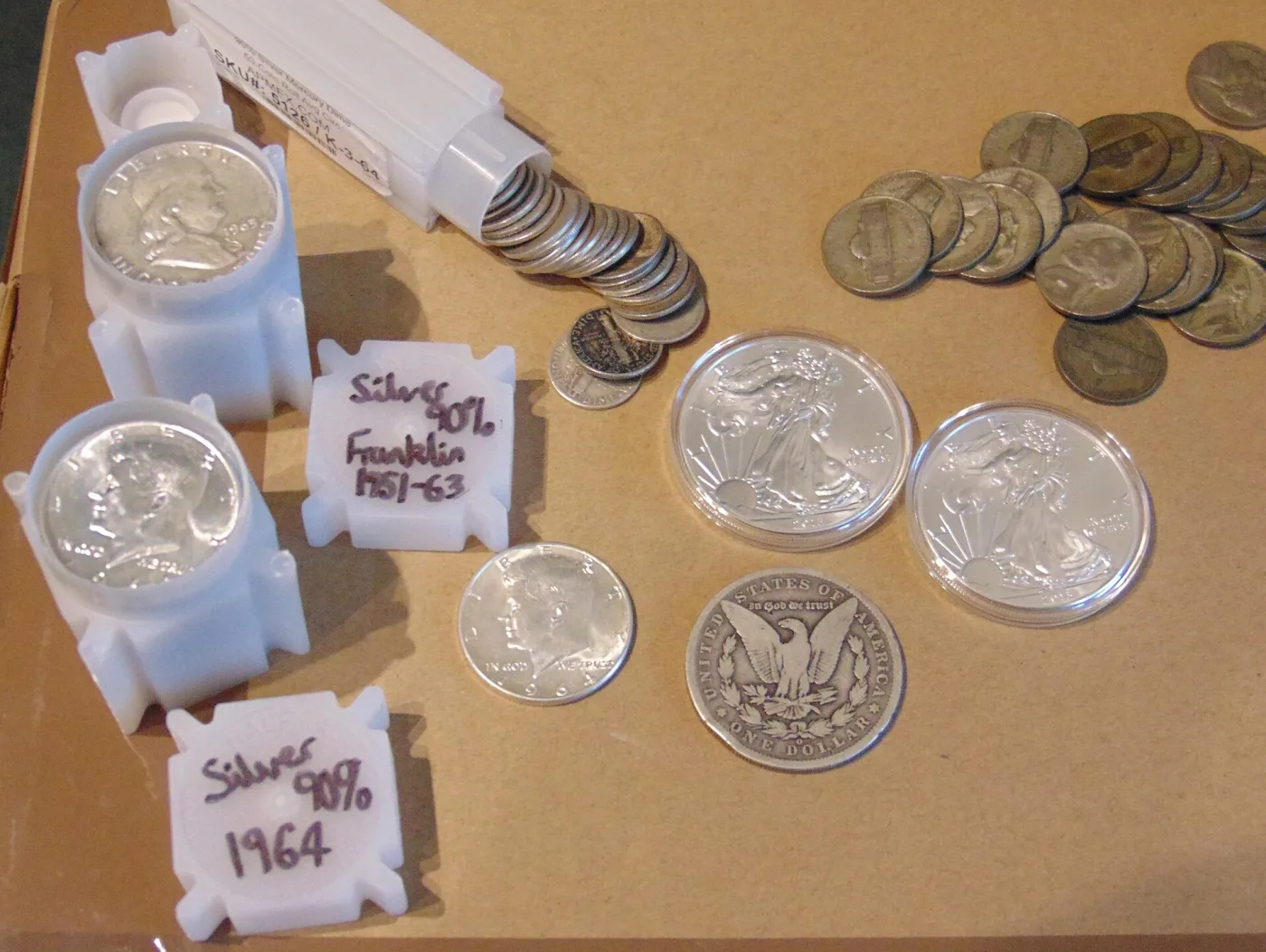 A junk silver holding on a tray: plastic tubes hand-labelled Silver 90% Franklin 1951-63 and Silver 90% 1964, a spilled tube of Mercury dimes, a loose 1964 Kennedy half, a Morgan dollar reverse, two encapsulated American Silver Eagles and a pile of copper-nickel Jefferson nickels