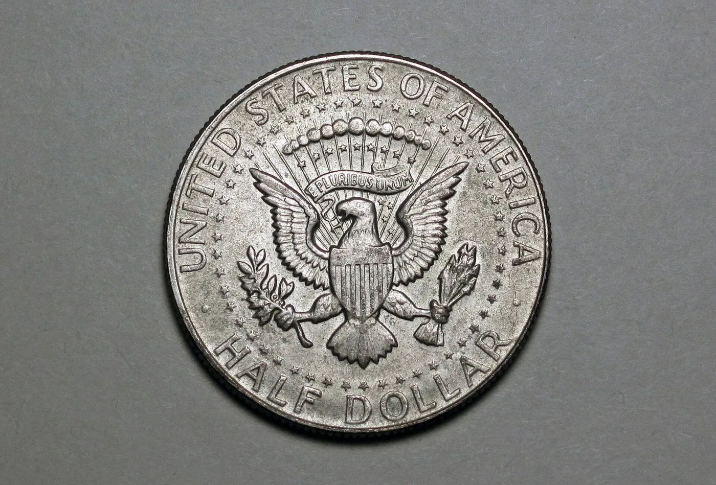 Reverse of a 1967 Kennedy half dollar showing the Presidential Seal eagle, the ring of fifty stars and the FG initials beside the eagle's leg