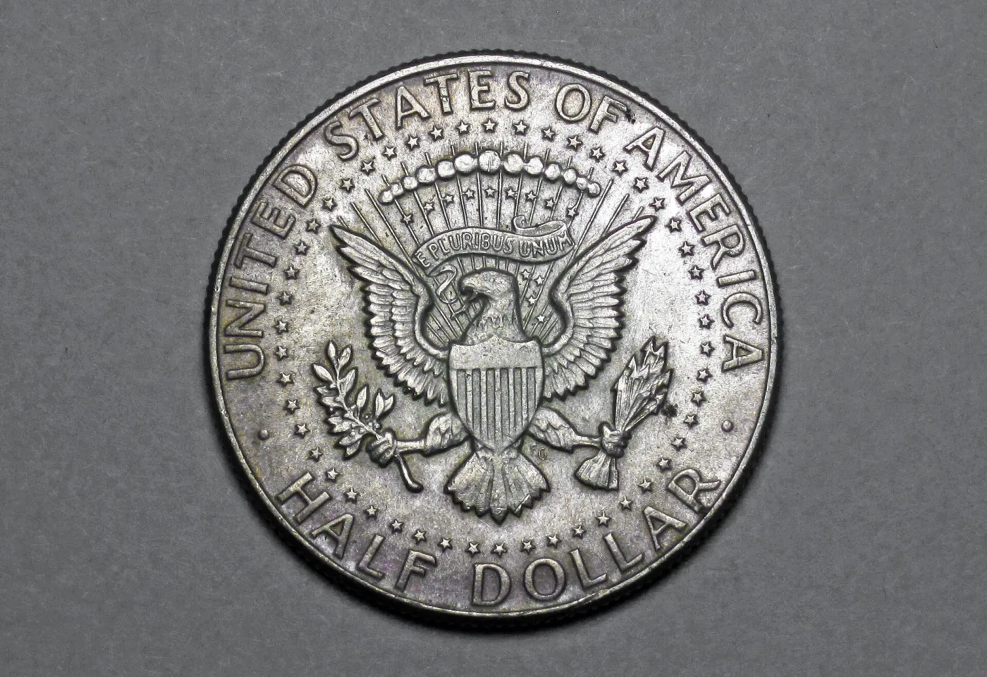 Reverse of the same 1964 Kennedy half dollar showing the Presidential Seal eagle and an empty field beside the olive branch where a mint mark would sit