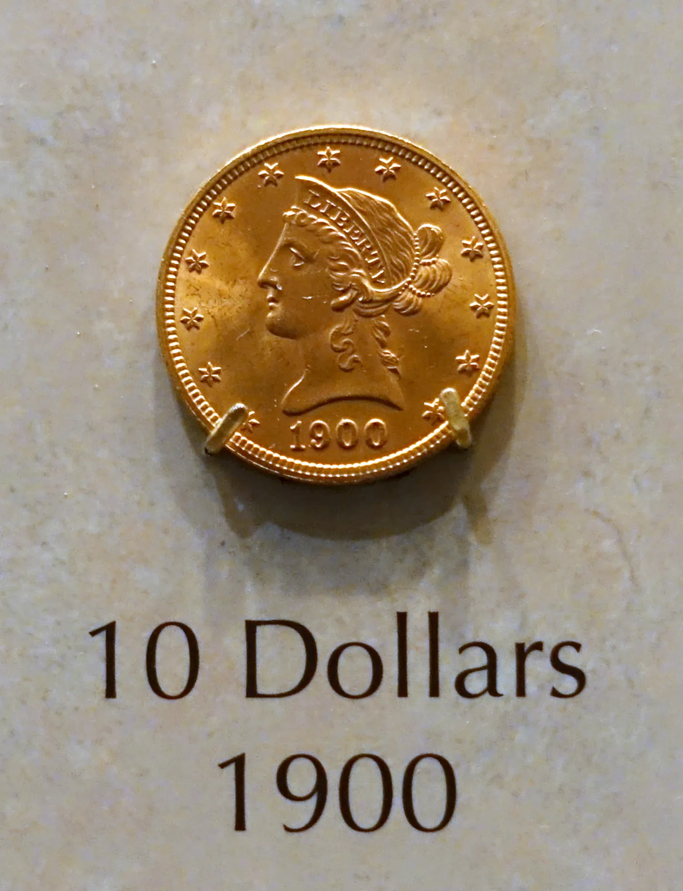 A 1900 Liberty Head Eagle mounted in a museum case above a printed label reading 10 Dollars 1900
