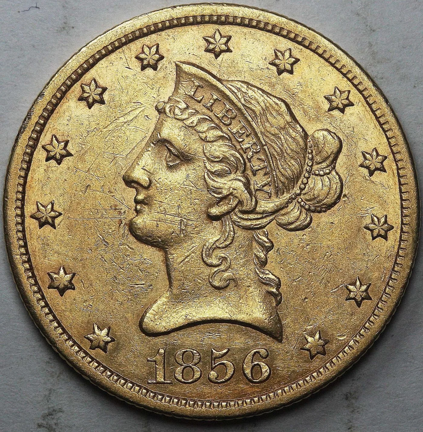Obverse of an 1856-S Liberty Head Eagle showing the coronet lettered LIBERTY, the beaded hair bun and a field covered in fine hairline scratches