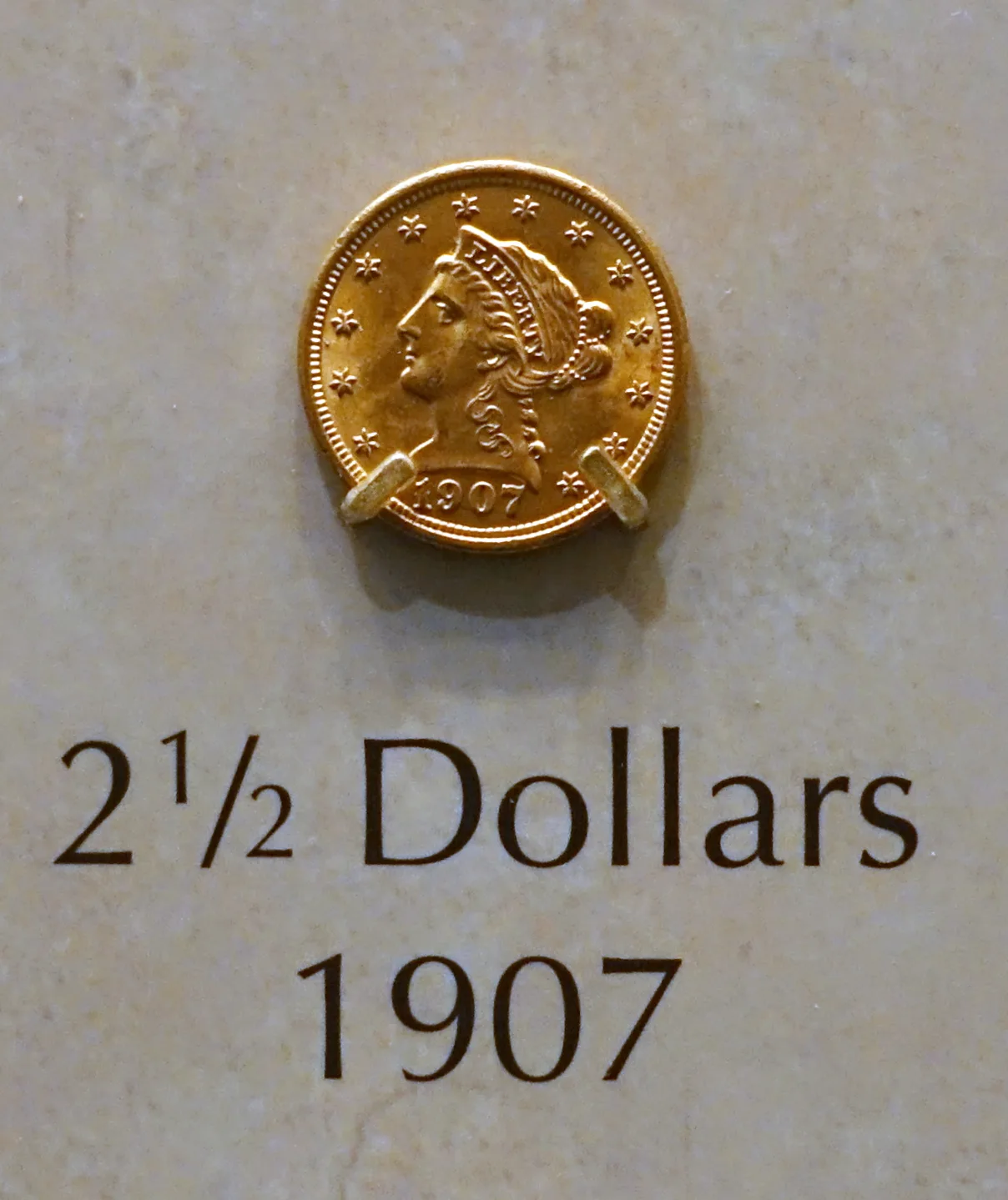 A 1907 Liberty Head Quarter Eagle mounted in a museum case above a printed label reading 2 1/2 Dollars 1907
