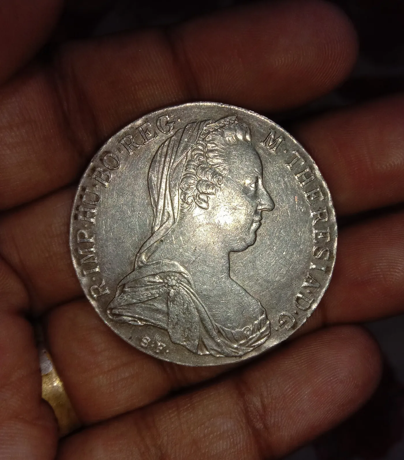Maria Theresa thaler obverse held in a palm, showing the veiled bust, the legend and S.F. below the shoulder, with light scratches across the fields