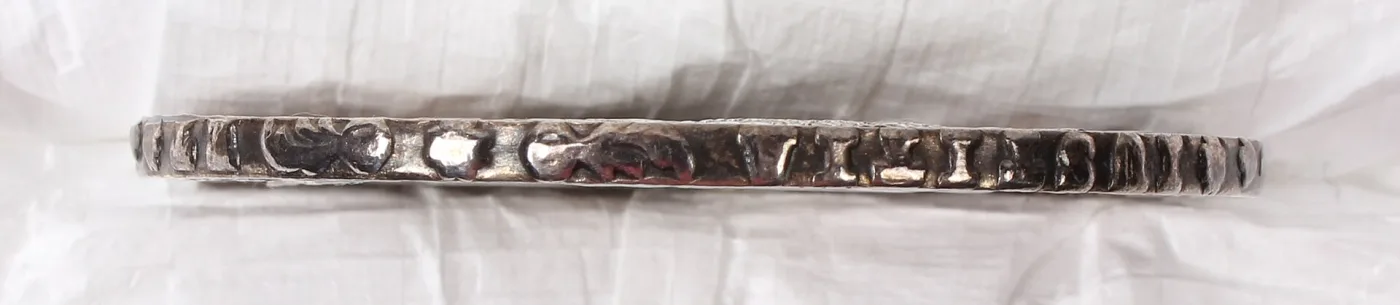 Edge of a 1780 Maria Theresa thaler seen side-on, showing raised letters and ornaments of the edge inscription