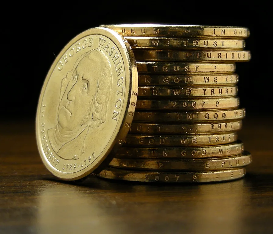 A stack of 2007-P George Washington dollars seen edge on, the incused edge inscriptions readable as IN GOD WE TRUST, E PLURIBUS UNUM and 2007 P, with one coin leaning against the stack showing the portrait