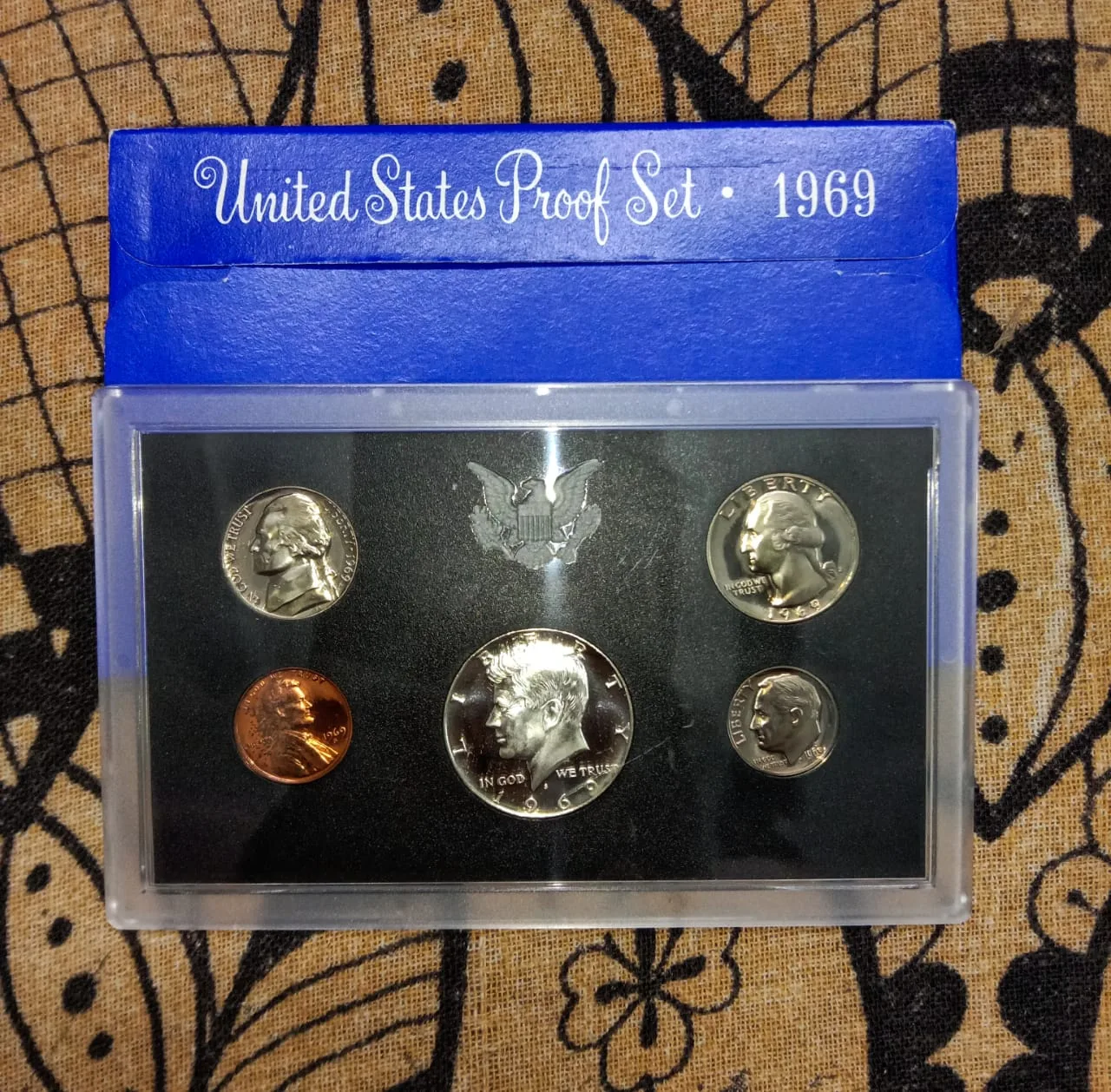 A 1969 United States Mint proof set in its blue sleeve, five proof coins sealed in a rigid clear lens over a black insert stamped with an eagle