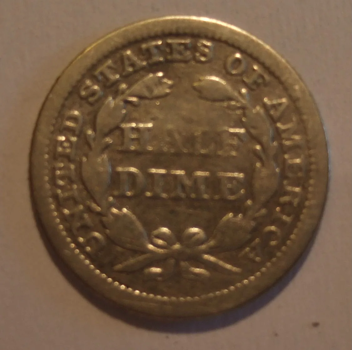 Heavily worn reverse of an 1853 Seated Liberty half dime, HALF DIME still readable inside a flattened laurel wreath with no mint mark
