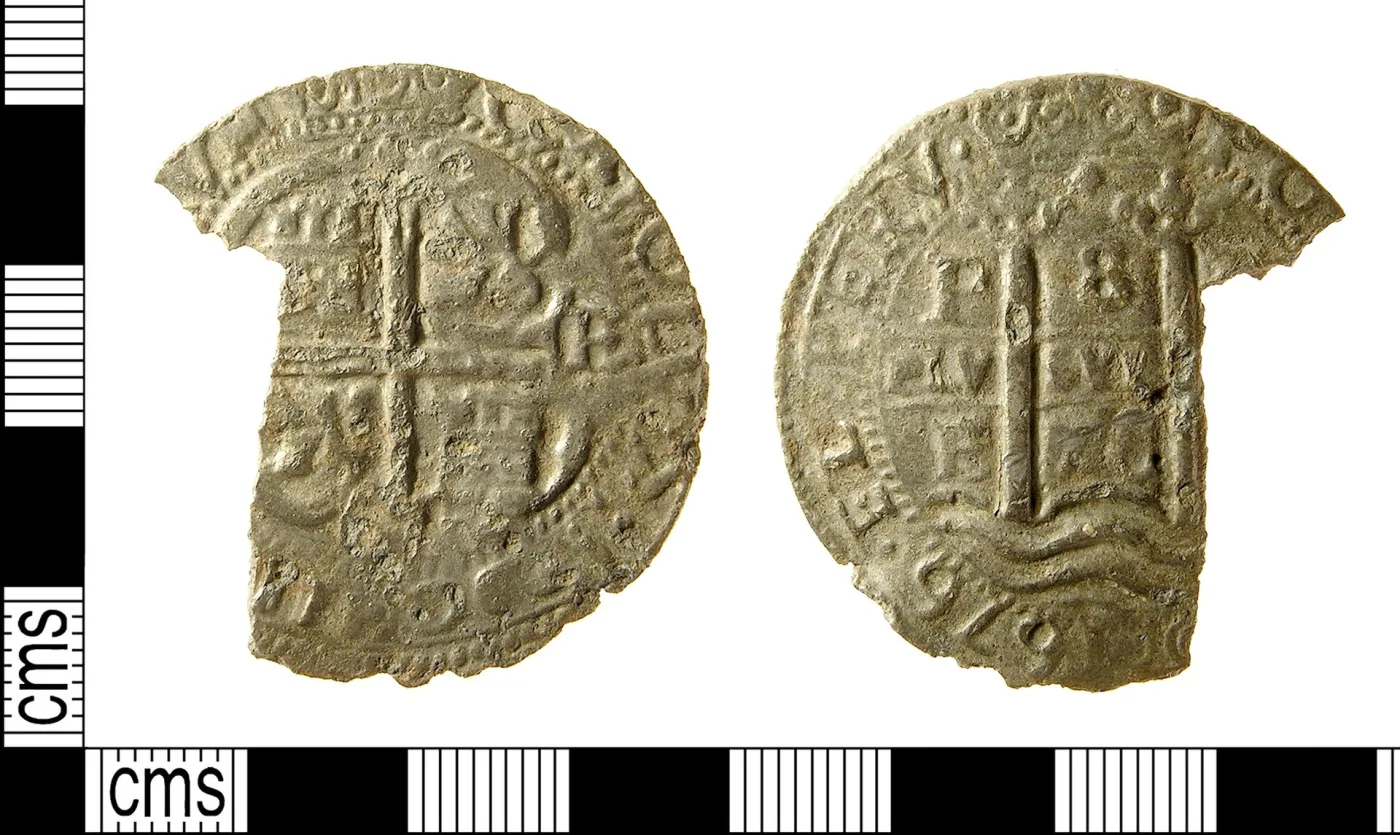 Obverse and reverse of a badly clipped silver cob photographed beside a centimetre scale, a cross design on one side and a pillar with wavy lines on the other