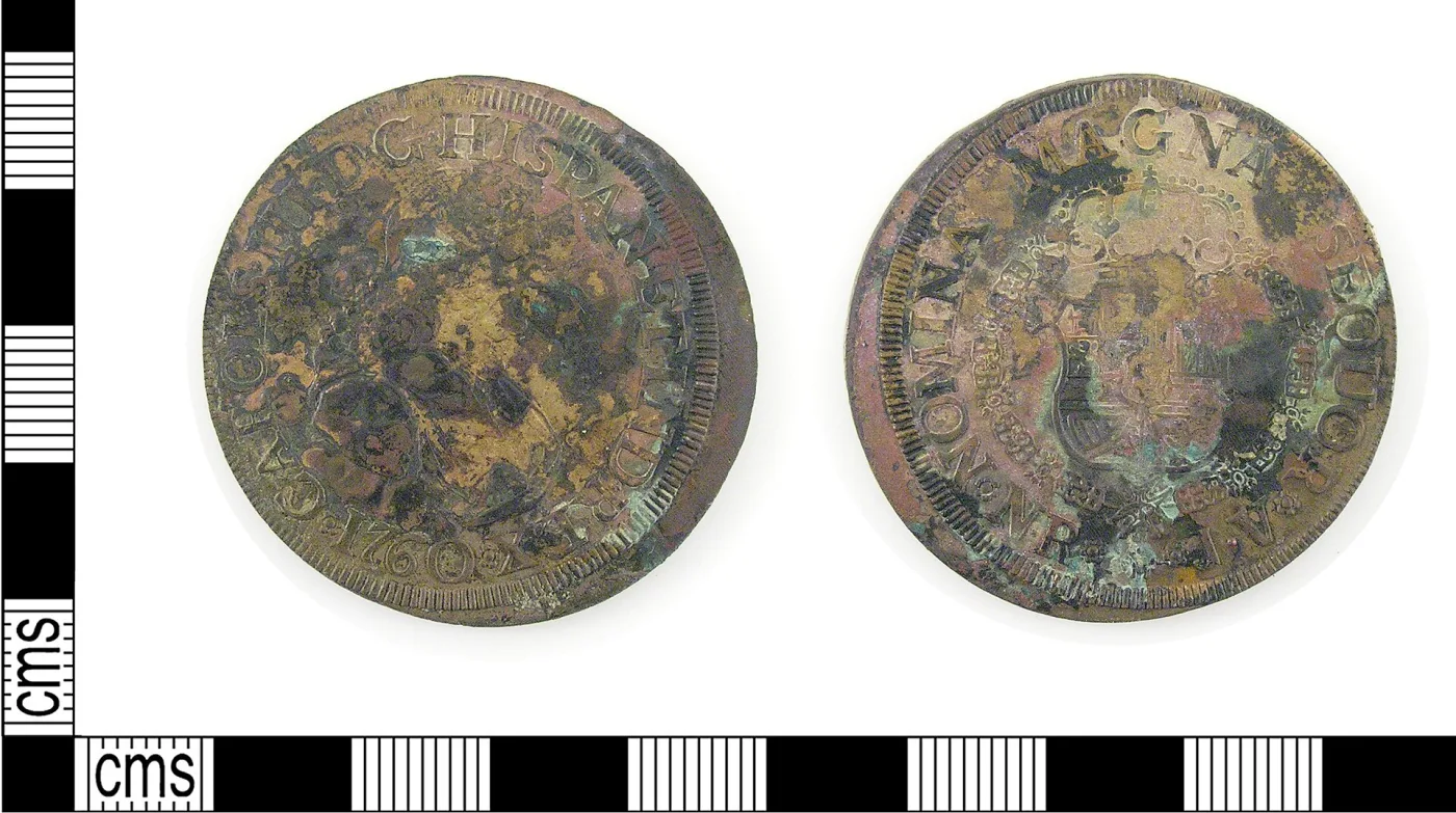 Obverse and reverse of a corroded coin-shaped disc showing the traces of a Spanish colonial design, the metal brown and green rather than gold
