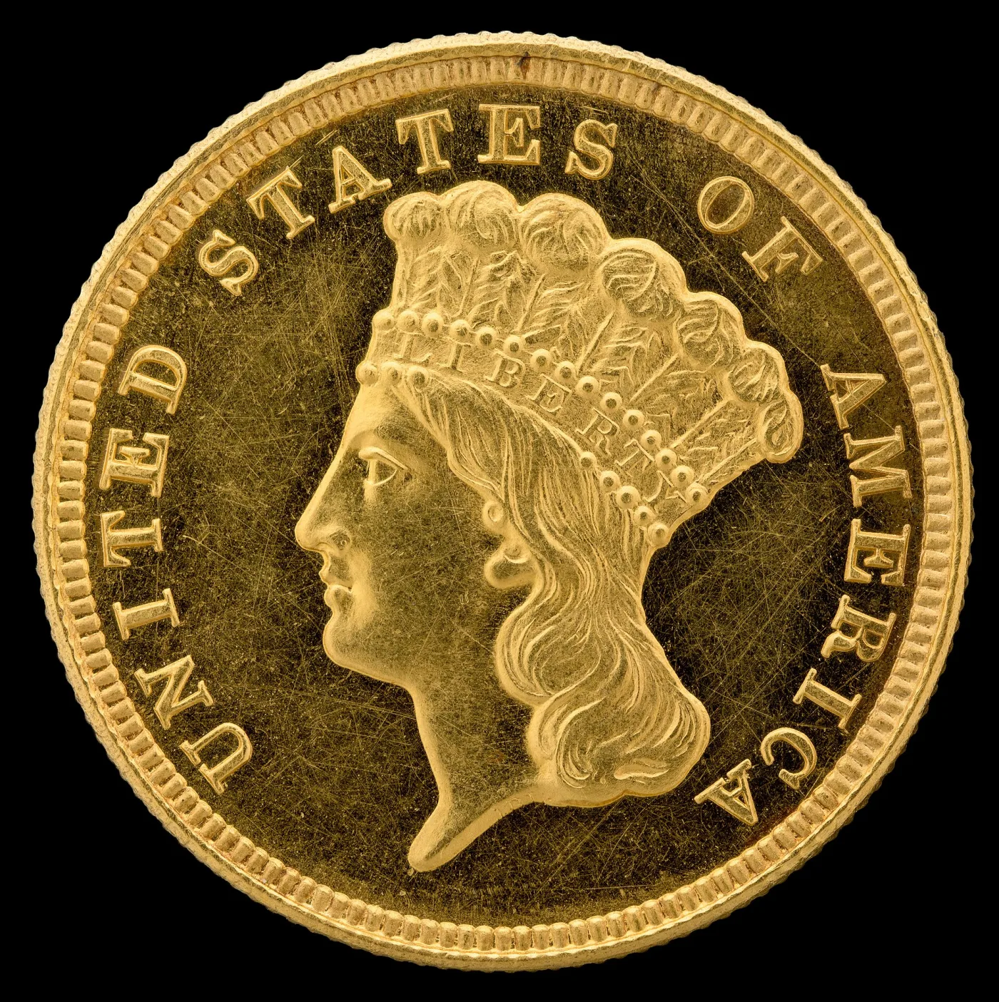 Obverse of a Three Dollar Gold piece: the Indian Princess facing left in a tall plumed headdress with LIBERTY across the beaded band, UNITED STATES OF AMERICA around a denticled rim, and no date on this side
