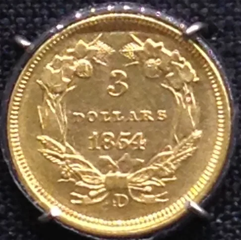 Reverse of an 1854 Three Dollar Gold piece with a D mint mark below the wreath bow and the word DOLLARS in wider, bolder letters