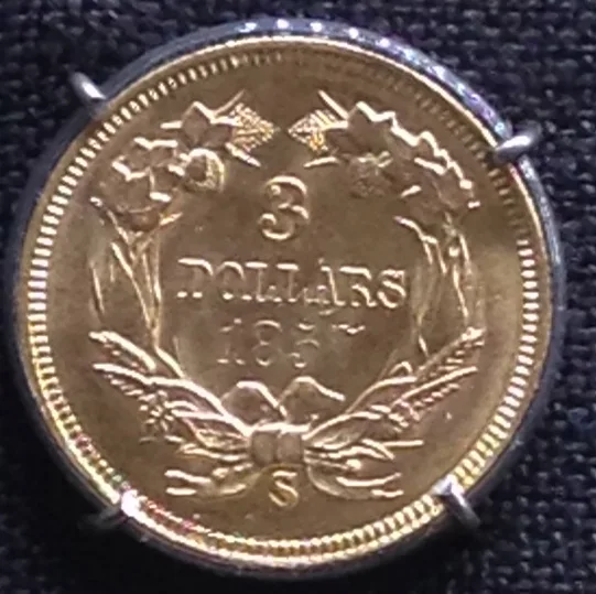 Reverse of a Three Dollar Gold piece with an S mint mark below the wreath bow and a date whose first three digits read 185