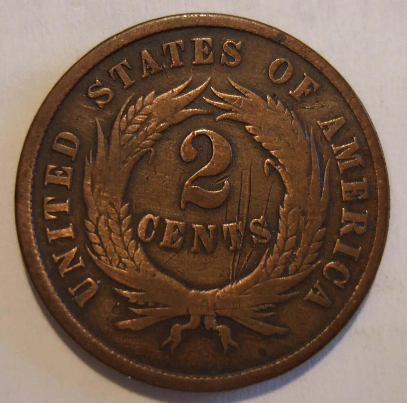 Reverse of a well-circulated 1865 two cent piece with the wheat heads worn flat and the ribbon bow reduced to an outline