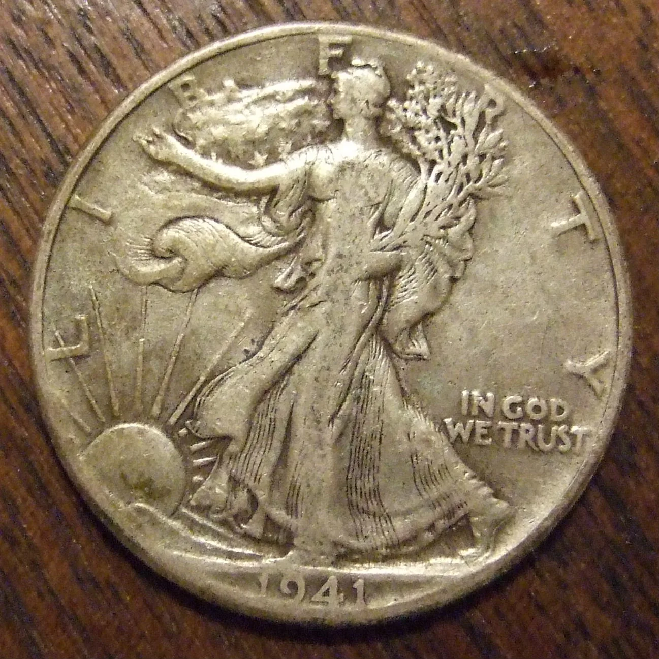 Obverse of a circulated 1941 Walking Liberty half dollar showing Liberty in a flag drape with laurel and oak branches in her left arm and the date below